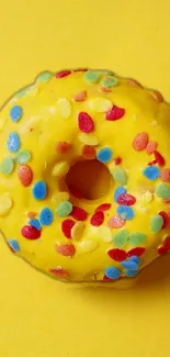 Colorful sprinkled donut on yellow background.