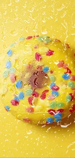 Bright yellow donut with colorful sprinkles on a wet yellow background.