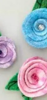 Felt flowers in blue, pink, and purple with green leaves.