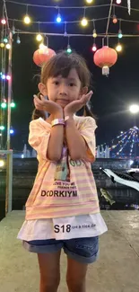 A child poses under colorful festival lights and lanterns at night.