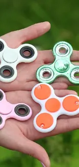 Four colorful fidget spinners on hands with green background.