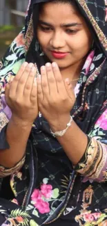 Woman in a colorful floral hijab, praying with serene expression.