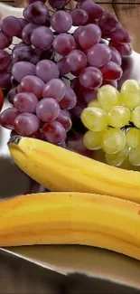 A vivid display of grapes, bananas, and apples on a reflective surface.