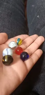 Colorful glass marbles in a hand with a dark fabric background.