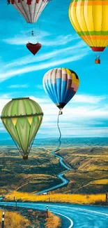 Colorful hot air balloons float over a winding road under a bright blue sky.