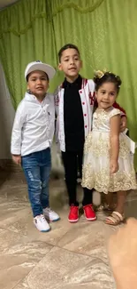 Three children posing indoors in colorful outfits with a green background.