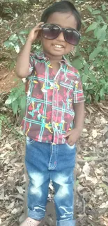 Smiling child in colorful outfit with sunglasses, standing outdoors.