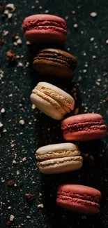 Assorted macarons on dark, textured background with crumbs.