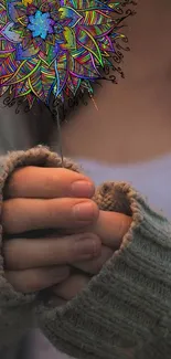 Person holding a colorful mandala flower with cozy sweater sleeves.