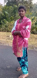 Woman standing outdoors in colorful attire with nature background.