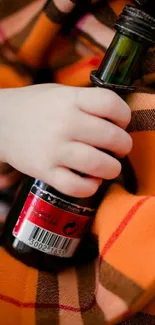 Hand holding a green bottle over orange plaid fabric with a cozy feel.