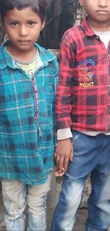 Two children in teal and red plaid shirts stand together.