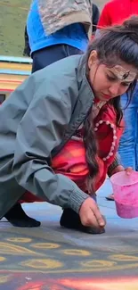 Woman creating colorful rangoli design on pavement with pastel colors.