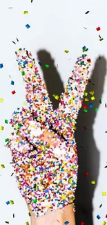 Hand making a peace sign covered in colorful sprinkles.