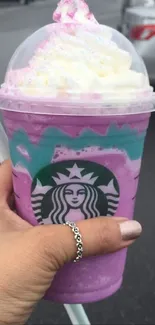 Hand holding a pink and blue unicorn frappuccino from Starbucks.