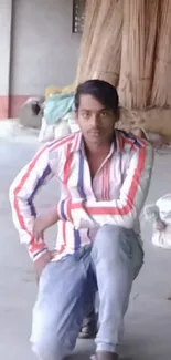 Person in colorful striped shirt kneeling indoors, with light gray background.