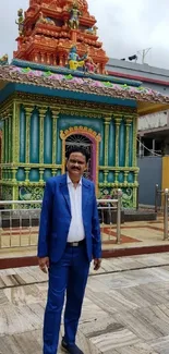 Man in blue suit standing before colorful temple.