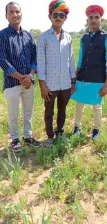 Three figures in colorful traditional attire stand outdoors in a lush green field.