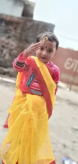 Child in vibrant yellow traditional attire, smiling outdoors.