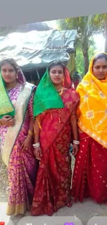 Three women in colorful sarees pose outdoors, showcasing vibrant traditional attire.