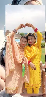 Two women in vibrant traditional attire making a heart shape.