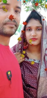 Couple in traditional attire with leafy backdrop.