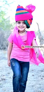 Child wearing colorful turban and pink clothes outside.