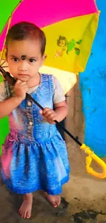 Child holding colorful umbrella in front of a vivid blue wall.