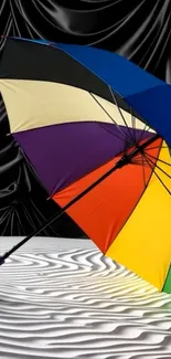 Colorful umbrella on sand with black drape background.