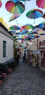 A vibrant street with colorful umbrellas hanging above cobblestone walkway.