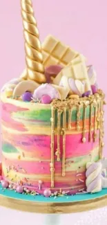 Colorful unicorn cake with gold and pastel decorations on a pink background.