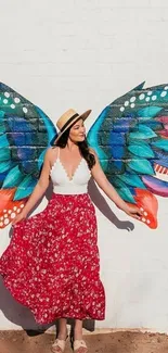 Woman poses with colorful wings against white brick wall.