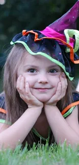 Young girl in colorful witch costume on grass.