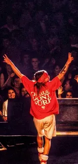 Performer in red shirt on stage with crowd cheering.