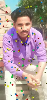 Man sitting with confetti background, wearing a purple shirt.