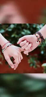 Two hands with colorful bracelets touching gently against a leafy background.