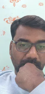 Thoughtful man with glasses, green floral backdrop.