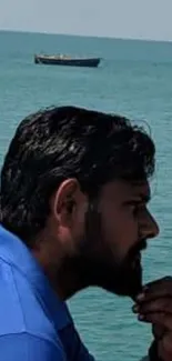 Man in profile by calm ocean with distant boat and blue horizon.