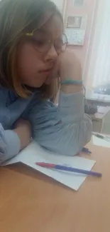 Student with glasses resting on desk, deep in thought.