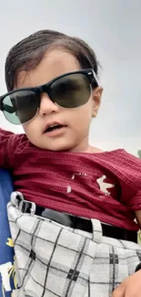 Adorable baby in sunglasses with burgundy shirt.