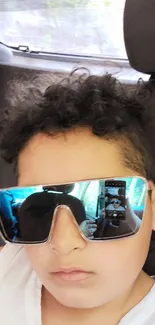 Young person with sunglasses reflecting image in car.