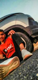 Young person in red shirt with car, urban setting.