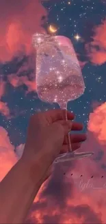 Hand holds galaxy-filled wineglass under a pink starry sky.