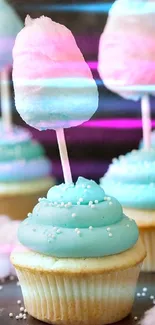 Cupcakes with blue frosting topped with pink cotton candy on a stick.