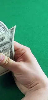 A hand counts hundred-dollar bills on a vibrant green surface.