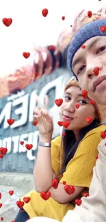 Young couple posing with heart emojis on a vibrant wallpaper.