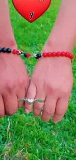 Couple holding hands with love bracelets on green grass background.