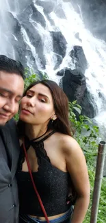 A couple standing before a majestic waterfall surrounded by lush greenery.