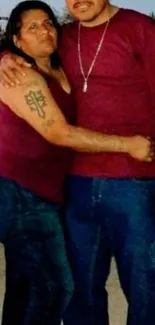 Couple standing together in matching maroon tops and blue jeans.