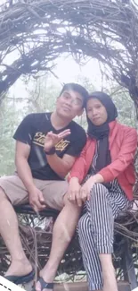 Couple sitting in a natural wooden nest, surrounded by greenery.